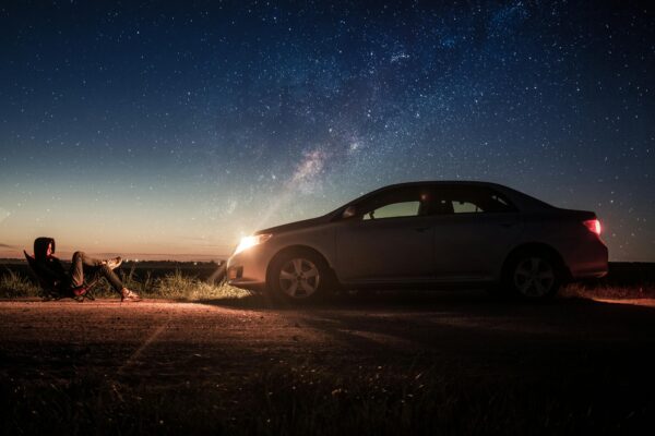 A person relaxes by their car under a starry night sky, capturing tranquility.